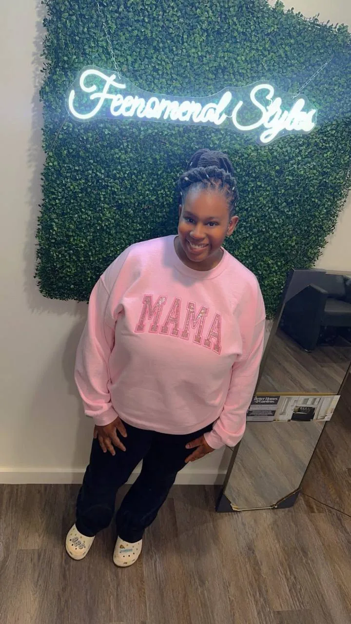 Client in a MAMA sweatshirt smiling in front of the hedge wall