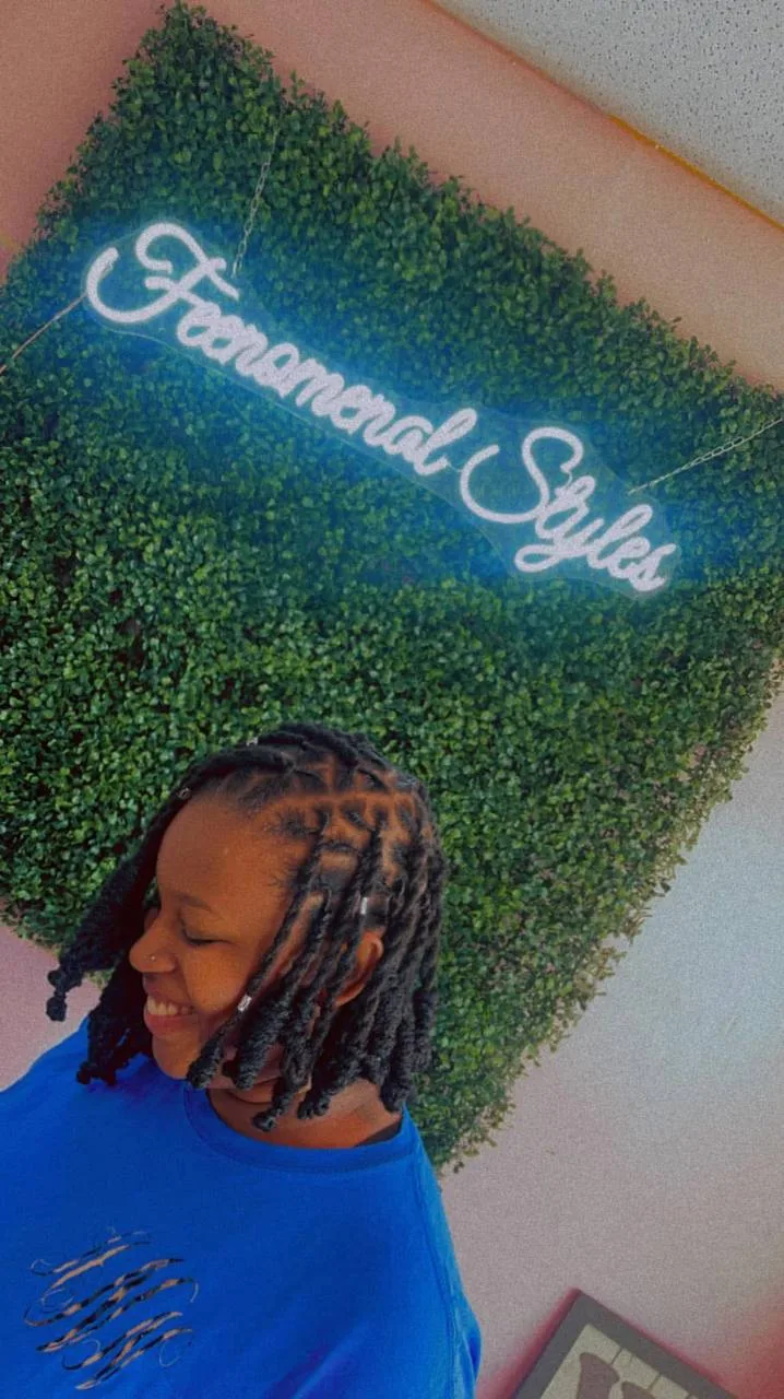 Young client with short styled locs under the neon sign