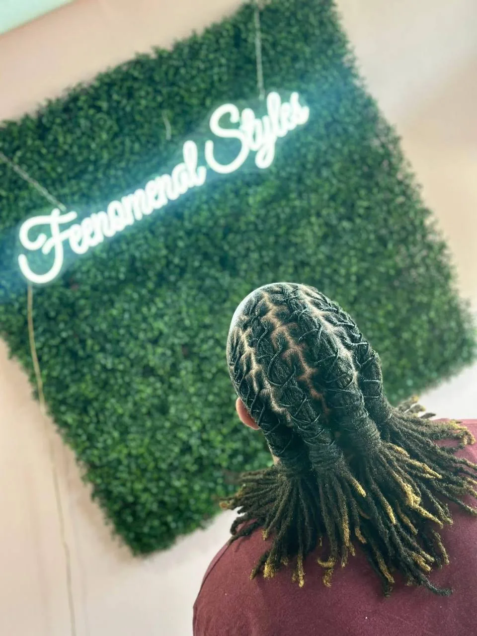 Back of a client's head with locs styled in a woven pattern under the neon